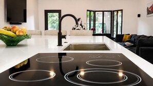 Une cuisine moderne équipée d’une plaque de cuisson à induction, d’un évier et d’un plan de travail sur lequel sont disposés des fruits.
