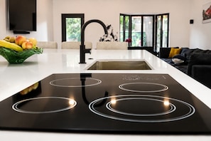 Una cocina moderna con una placa de inducción, un fregadero y una encimera con frutas.
