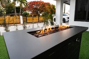 Una chimenea exterior moderna con un diseño negro elegante, rodeada por un césped cuidado y una valla de madera.