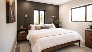 Une chambre moderne avec un grand lit, des murs de couleur sombre et une fenêtre laissant entrer la lumière naturelle.