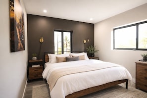 Un dormitorio moderno con una cama grande, paredes oscuras y una ventana que proporciona luz natural.