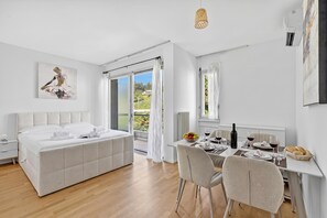 A modern bedroom with a large bed, a dining area with a table set for two, and a sliding glass door leading to a balcony. - Smart Stay Lugano, Lugano, Switzerland (Lugano)
