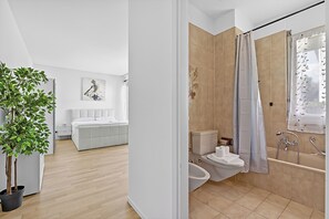 Ein modernes Badezimmer mit einer Badewanne, Toilette und einem Bidet. Eine Topfpflanze und ein Bild sind an der Wand angebracht.