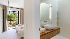 Un dormitorio moderno con un ventanal grande, una cama, una mesita de noche y un baño con lavamanos y espejo.