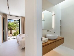Ein modernes Schlafzimmer mit großem Fenster, einem Bett, einem Nachttisch und einem Badezimmer mit Waschbecken und Spiegel.