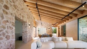 Un interior moderno con paredes de piedra, techo de madera y un amplio sofá blanco.