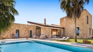 Un edificio de piedra con piscina, mobiliario exterior y palmeras.