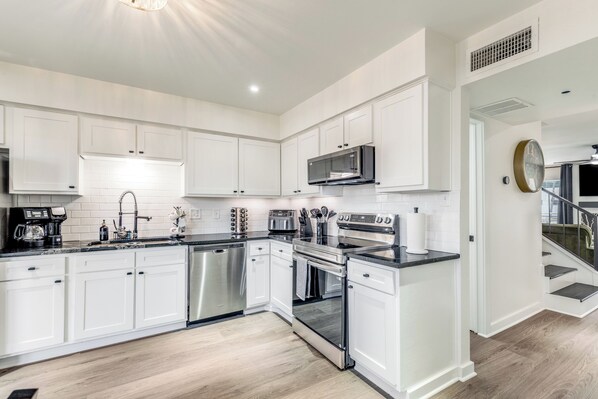 A modern kitchen with white cabinetry, stainless steel appliances, and a black countertop.