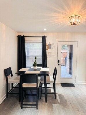Un coin repas avec une table et des chaises, une plante en pot et une porte donnant sur un jardin.