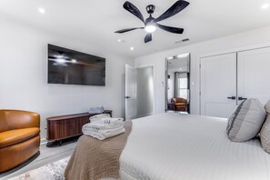 Un dormitorio moderno con una cama, un sillón de cuero, una mesita de madera, un televisor de pantalla plana y un ventilador de techo.