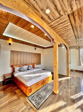 A bedroom with a wooden bed, a nightstand, a patterned rug, and a wooden ceiling structure.. ORCHARD VALLEY RESORT