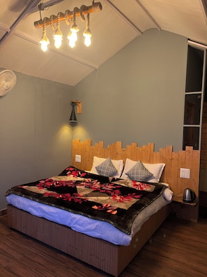 Un dormitorio con cabecera de madera, cama con ropa de cama floral, lámpara de pared y ventilador de techo.
