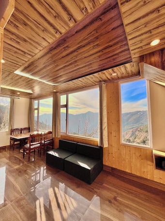 A room with wooden ceiling, large windows with mountain views, a dining table with chairs, and a black sofa.. ORCHARD VALLEY RESORT