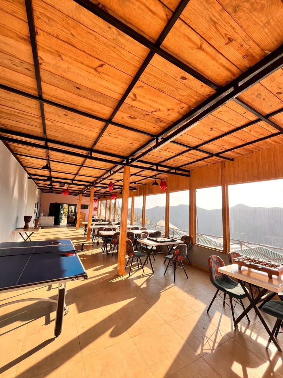 Una habitación amplia con techo de madera, ventanas grandes y una mesa de ping pong.