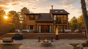 Une cabane en rondins à deux étages, dotée d’un patio en pierre, d’un espace salon extérieur et d’un foyer.