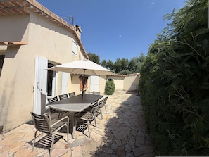 Eine Terrassengruppe mit Tisch und Stühlen, einem weißen Sonnenschirm und einem gepflasterten Weg.