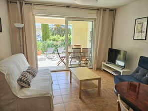Ein Wohnzimmer mit einer Couch, einem Fernseher, einem Couchtisch und einem Balkon mit Stühlen und einem Tisch.