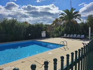 Ein Schwimmbecken mit gefliestem Sonnendeck, Liegestühlen und einem eingezäunten Bereich mit Palmen.