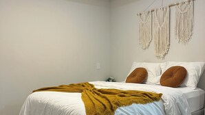 Ein Schlafzimmer mit einem Bett, einer Wanddeko aus Makramee und einem Holzboden.