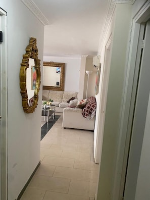 A hallway leading to a living area with a white sofa, a decorative mirror, and a floor lamp. - EXECUTIVE ROOM PUNTA PAITILLA WITH WIFI PLUG IN BED (Panamá)