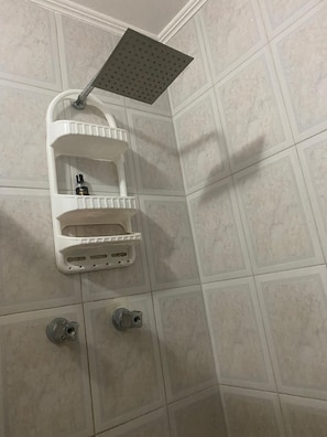 Eine Dusche mit einer eckigen Duschbrause, ein weißes Ablagebrett mit einer Flasche und zwei Wasserhähnen.