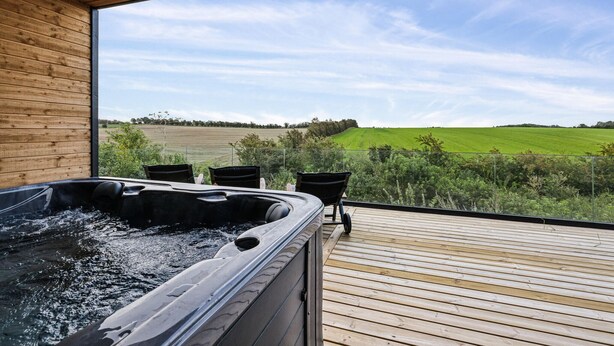Un bain à remous sur une terrasse en bois, avec vue sur un champ verdoyant.