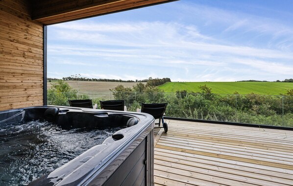 Ein Whirlpool auf einer Holzterrasse mit Blick auf ein grünes Feld.