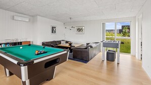 Une table de billard, un canapé et une table de baby-foot se trouvent dans une pièce donnant sur l’extérieur.