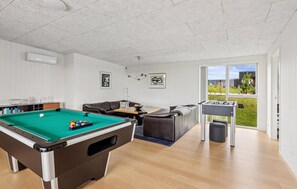 Ein Billardtisch, eine Couch und ein Kicker befinden sich in einem Raum mit Blick ins Freie.