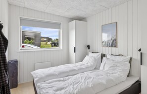 Ein Schlafzimmer mit Bett, Fenster, Tür und einem gerahmten Bild an der Wand.