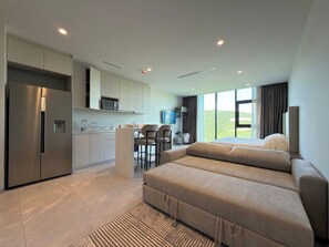 A modern kitchen with a built-in refrigerator, a dining area with a bar stool, and a sofa in a living area with a view of the outdoors.