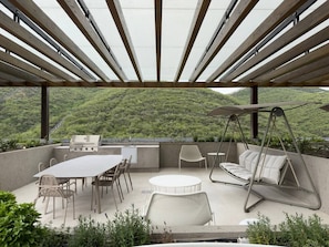 A covered outdoor patio with a table, chairs, a swing, and a grill.