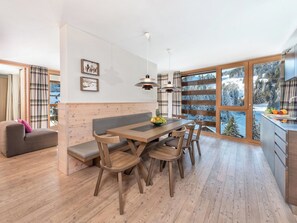 A modern kitchen with wooden cabinetry, a dining area with a wooden table and chairs, and large windows with a snowy landscape view.