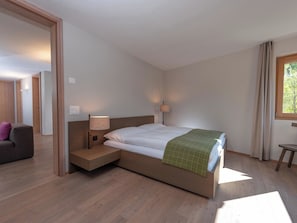Un dormitorio moderno con una cama de madera, mesitas de noche, una lámpara, un sofá y una ventana con cortinas.