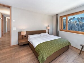 Ein Hotelzimmer mit einem Bett, Nachttischlampen, einem Fenster mit Blick auf eine verschneite Landschaft und Holzböden.