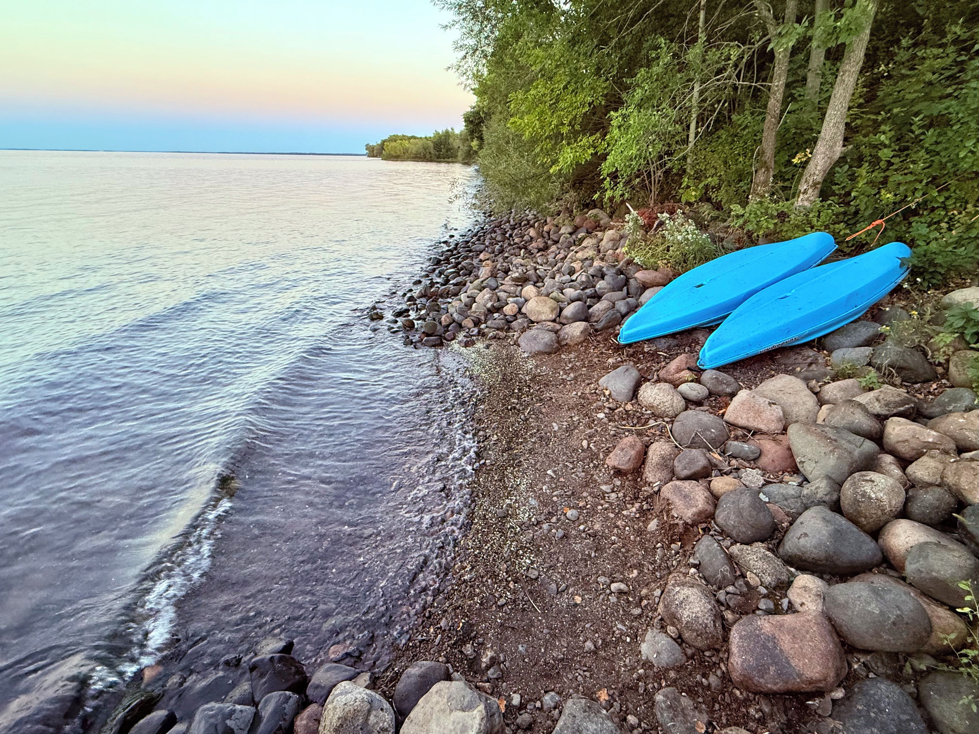 Une côte rocheuse bordant une étendue d’eau calme, avec des arbres et deux kayaks bleus.