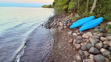 Une côte rocheuse bordant une étendue d’eau calme, avec des arbres et deux kayaks bleus.