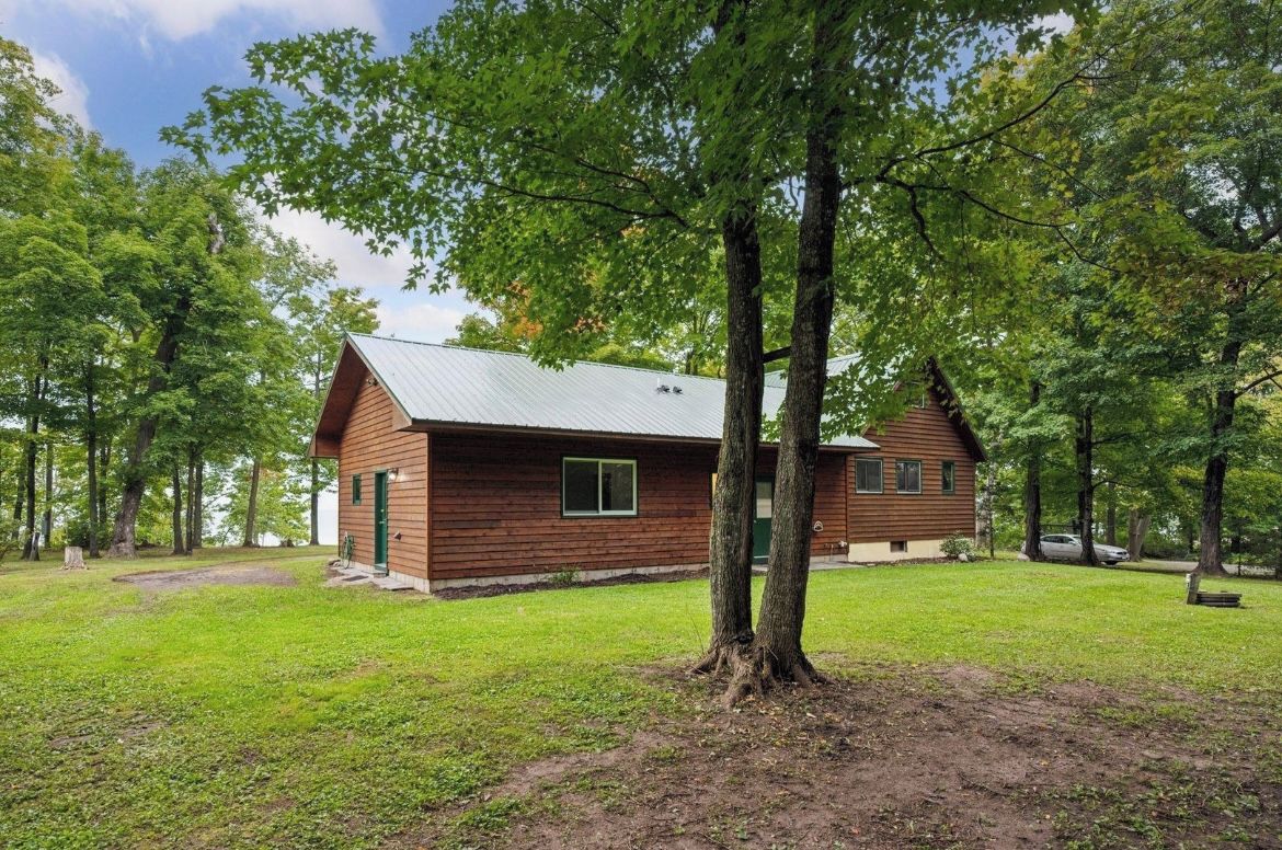 Une cabane en bois avec un toit en métal, entourée d’arbres et d’une zone herbeuse.