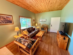 Una habitación acogedora con un sofá, una mesa de centro de madera, una silla, un mueble para televisor y una puerta.