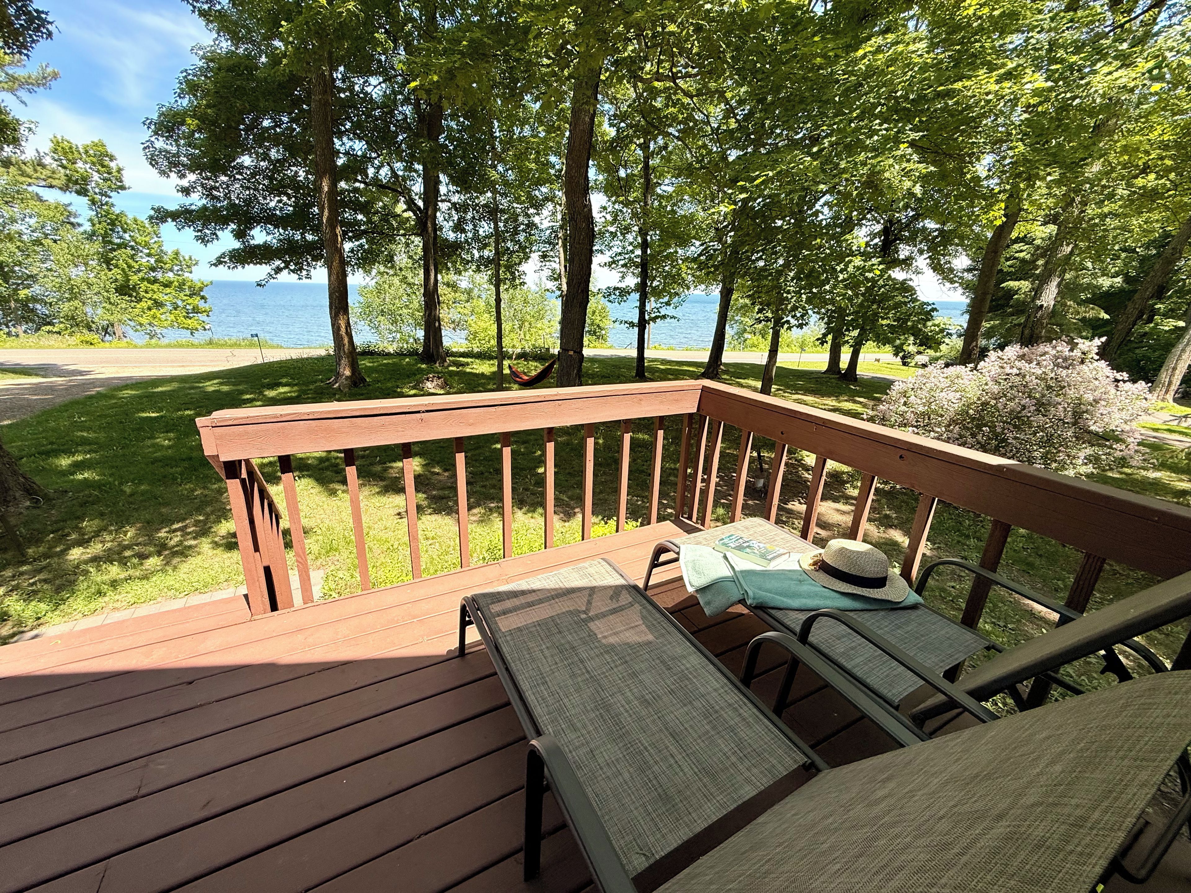 Une terrasse en bois avec une table et des chaises, donnant sur une pelouse et un plan d’eau.