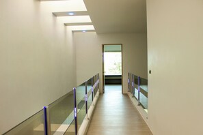 Passadís amb baranes de vidre, sòl de fusta i una porta que dona a una zona lluminosa.