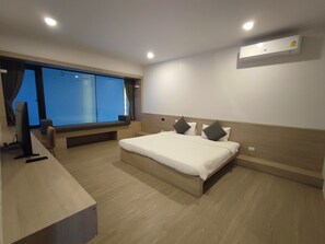 Habitació d'hotel moderna amb un llit gran, una taula de treball, un ordinador i una finestra amb cortines.