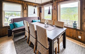 Ein Essbereich mit einem Holztisch, Korbstühlen und einer Couch mit Türkis-Kissen.