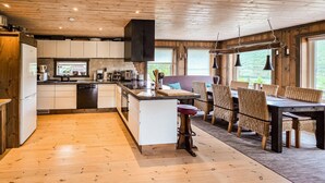 A modern kitchen with wooden cabinets, a central island, and a dining area with wicker chairs and a table. - Amazing home in Hovet with sauna (Hovet)