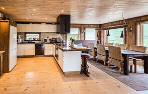 Eine moderne Küche mit Holzschränken, einer zentralen Kochinsel und einem Essbereich mit Korbstühlen und einem Tisch.