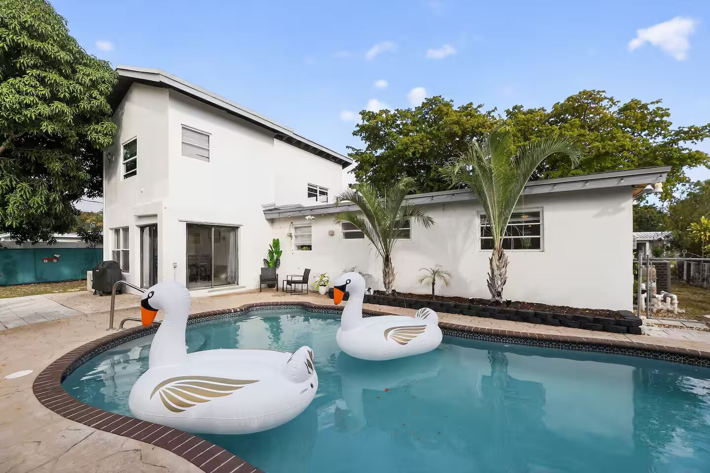 A swimming pool with two swan-shaped inflatable toys, a white building, and surrounding greenery.