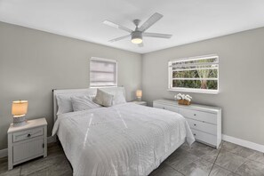 Ein Schlafzimmer mit einem Bett, Nachttischen, einem Deckenventilator, einem Fenster mit Blick und einer Kommode.