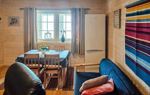 Ein gemütliches Zimmer mit Esstisch, Stühlen, einer Couch, einem farbenfrohen Teppich und einem Fenster mit Vorhängen.