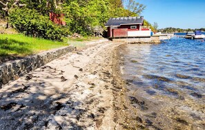 A beach with a wooden structure, clear water, and boats in the background. - Beautiful home in Stathelle with house sea view (Stathelle)