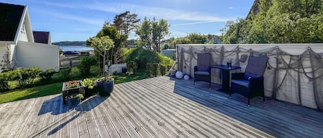A wooden deck with outdoor furniture, a white building, and a view of a body of water.